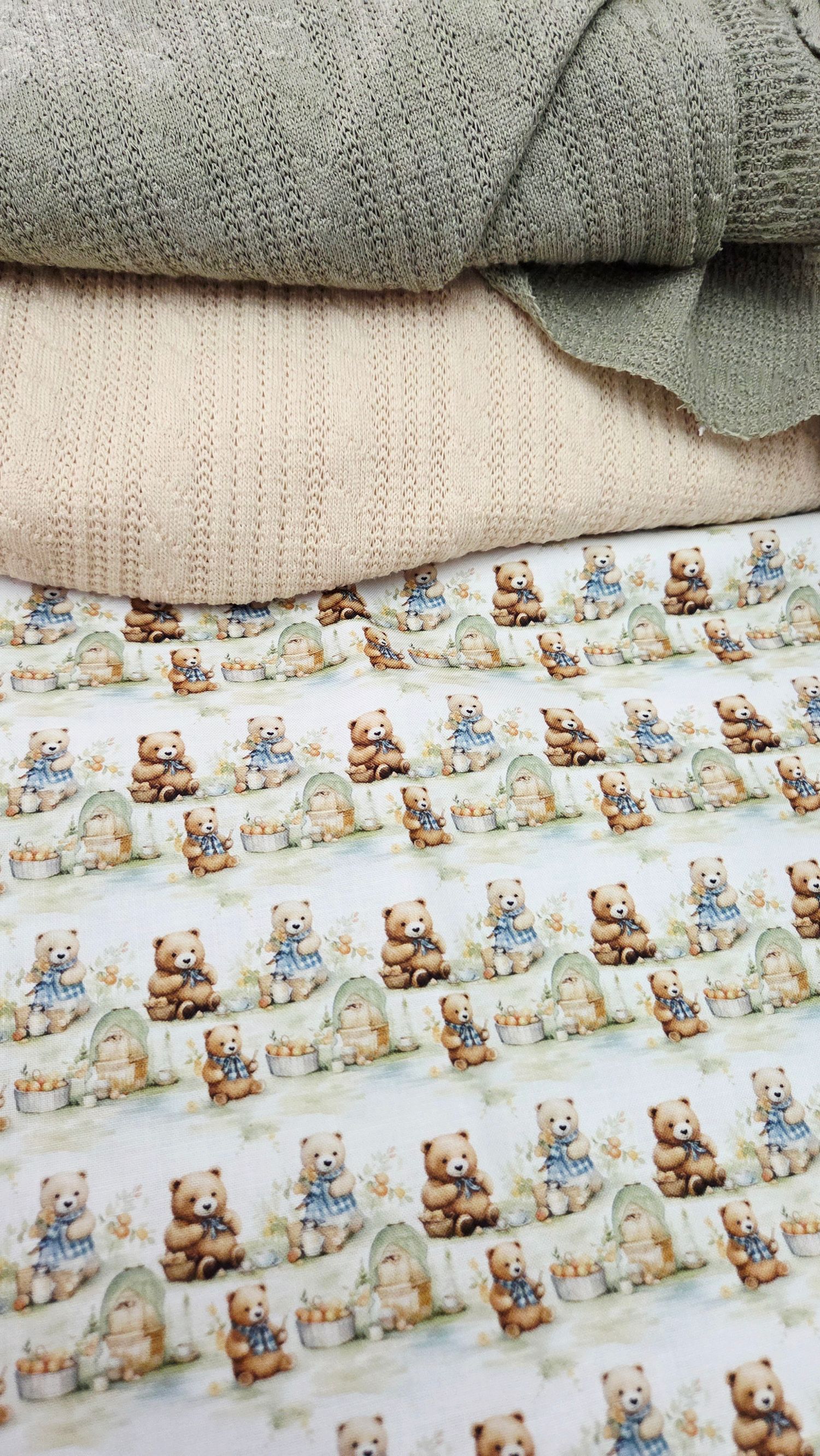 Stacked knit baby blankets in sage green and cream beside teddy bear printed fabric featuring charming bears with honey pots.
