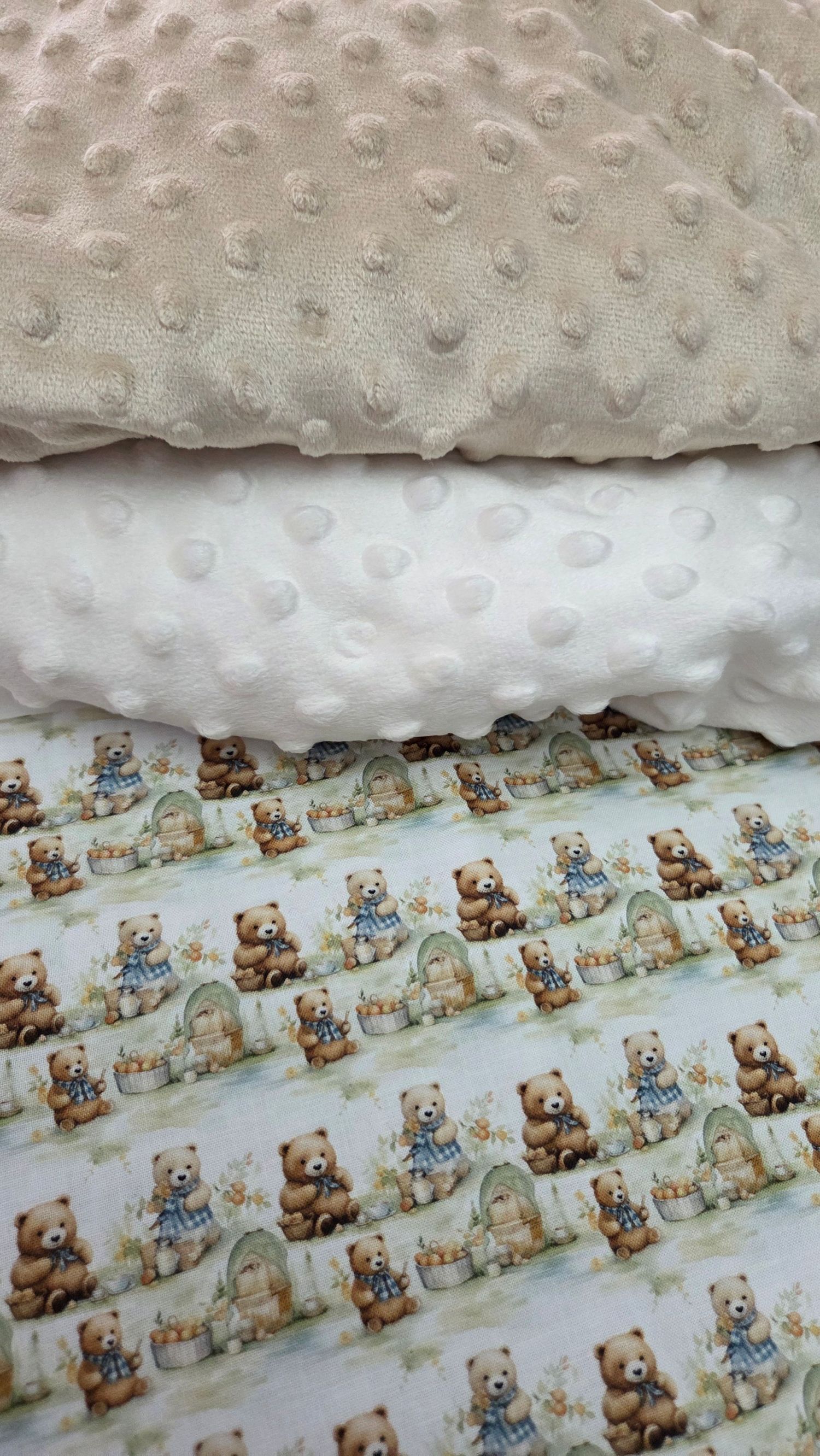 Three stacked fabric swatches featuring beige and white minky dot textures on top and a cute teddy bear print on the bottom.