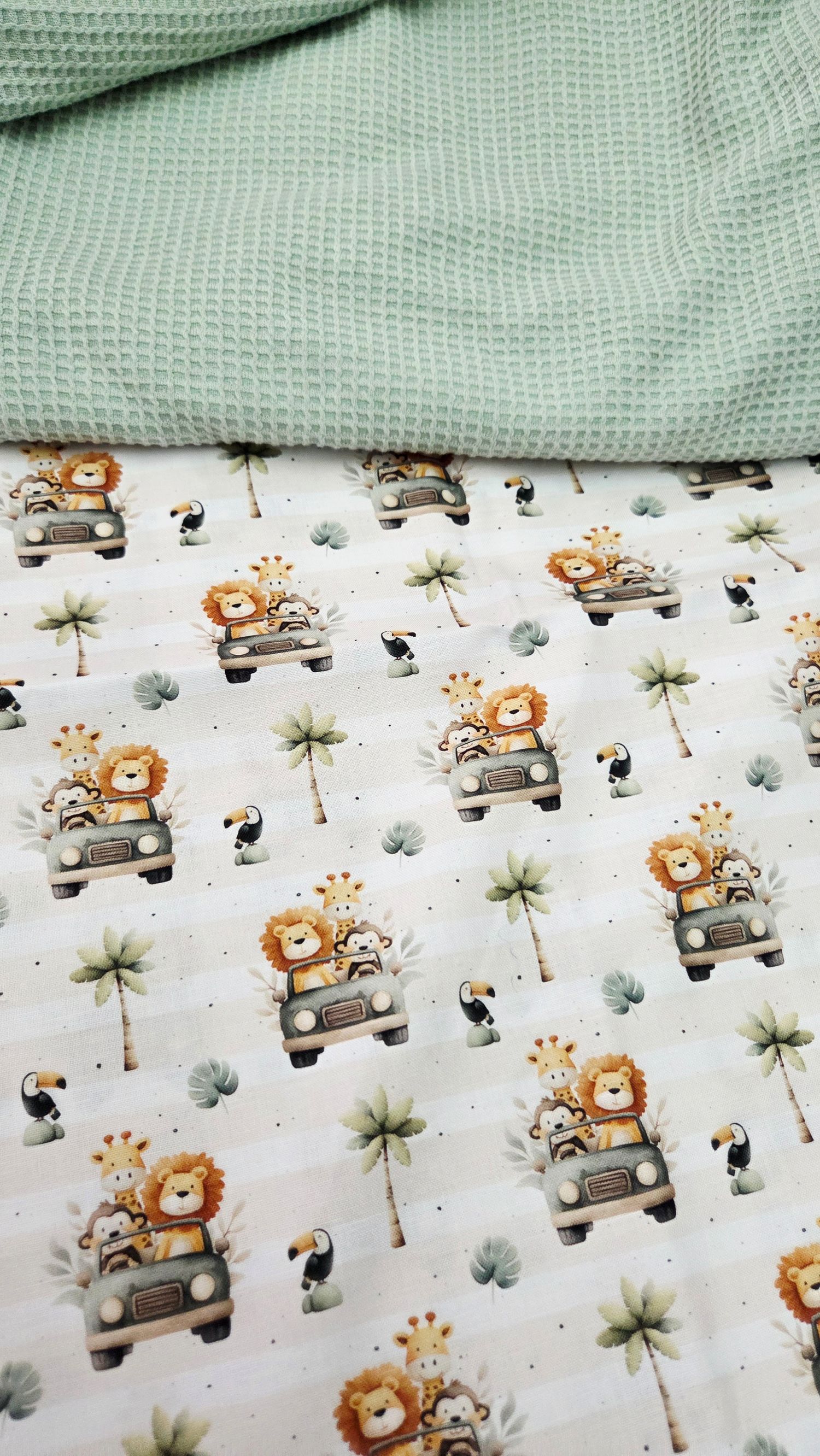 Two fabrics stacked: mint green waffle knit on top, white cotton print with safari animals in jeeps, giraffes, and toucans below.