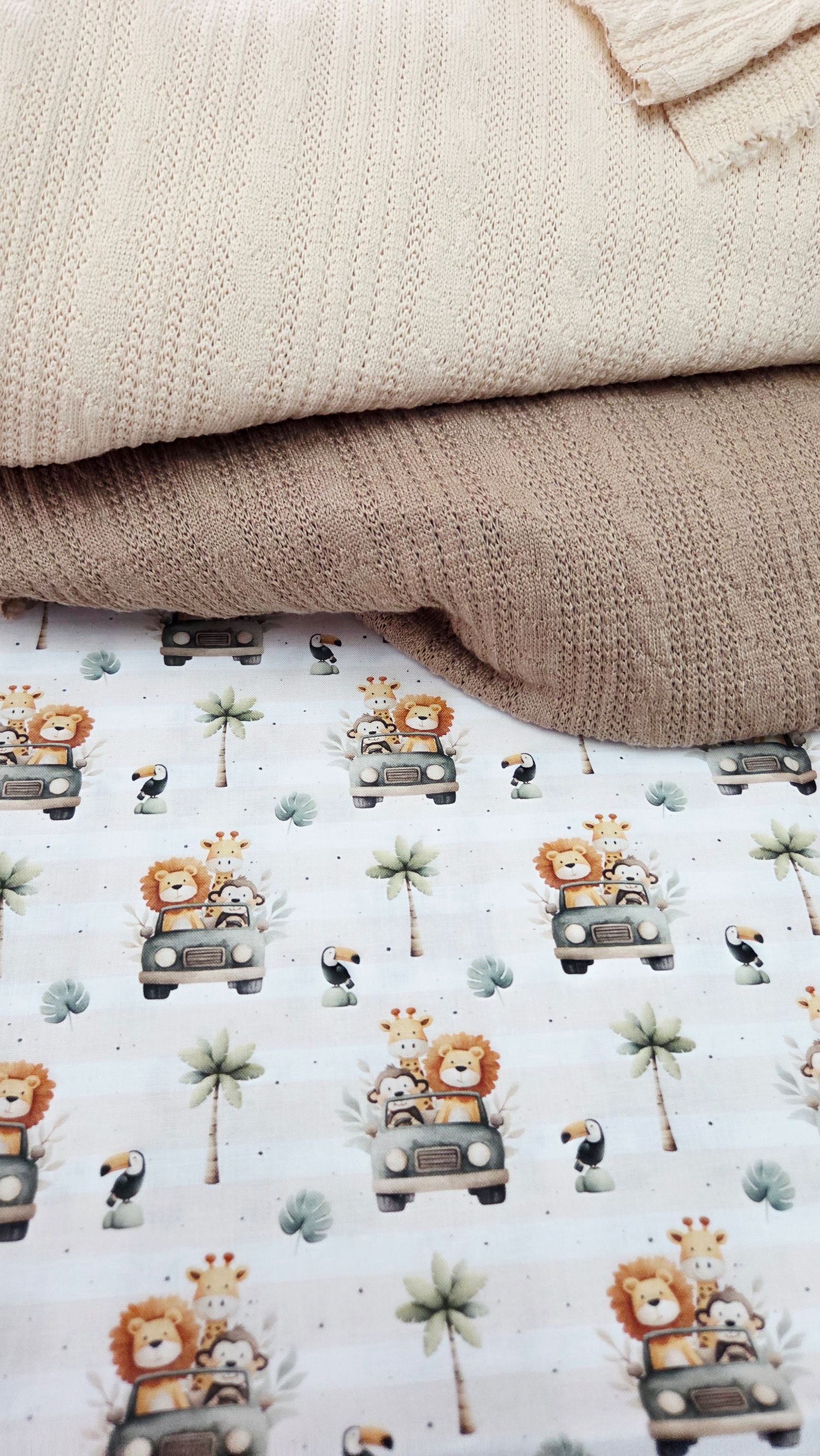 Stacked beige knit blankets beside a white safari-themed fabric featuring lions, giraffes, and toucans in jeeps.
