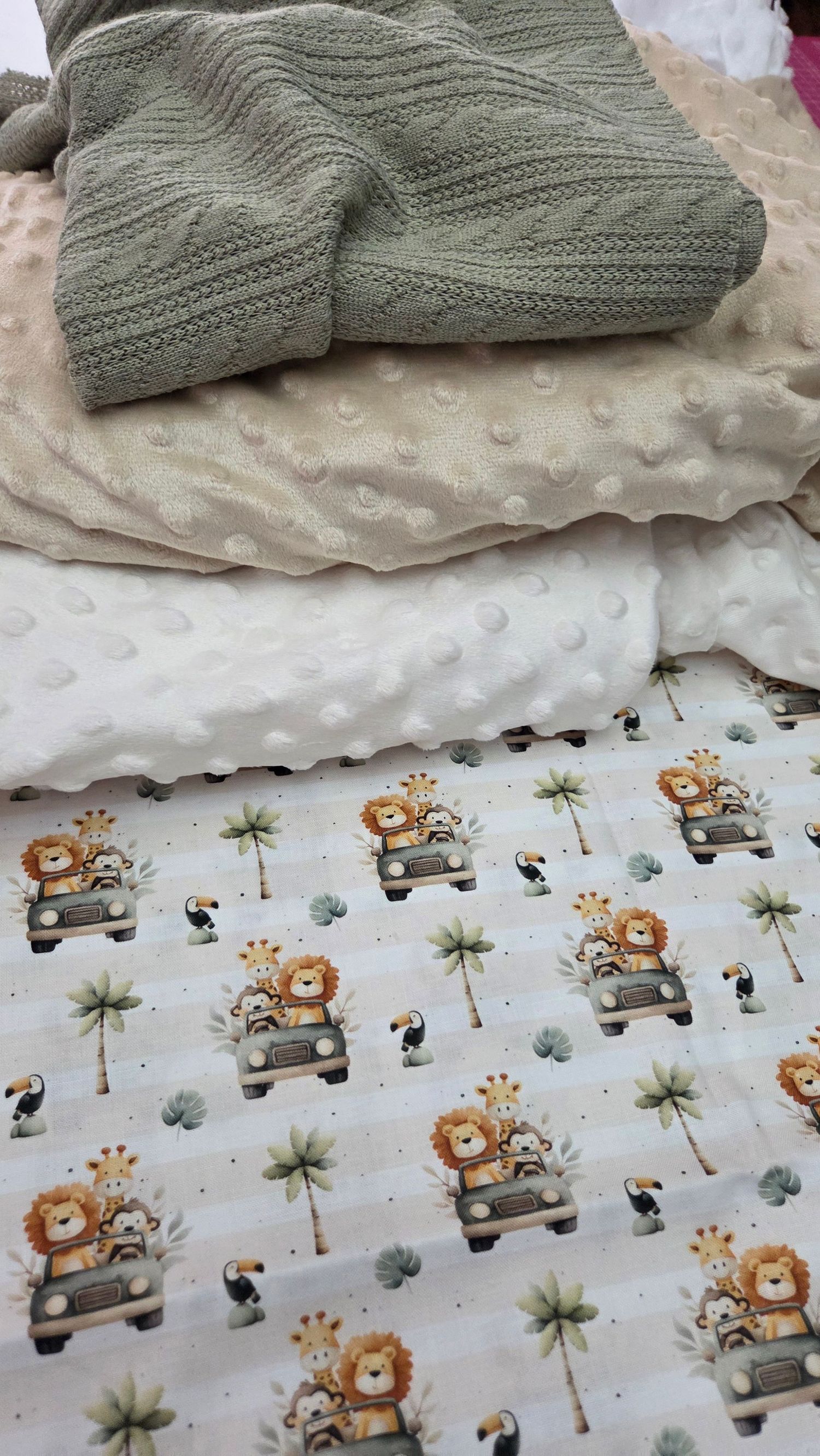 Stacked baby blankets featuring safari animal print with lions and giraffes, white minky dot, and sage green knit layers.
