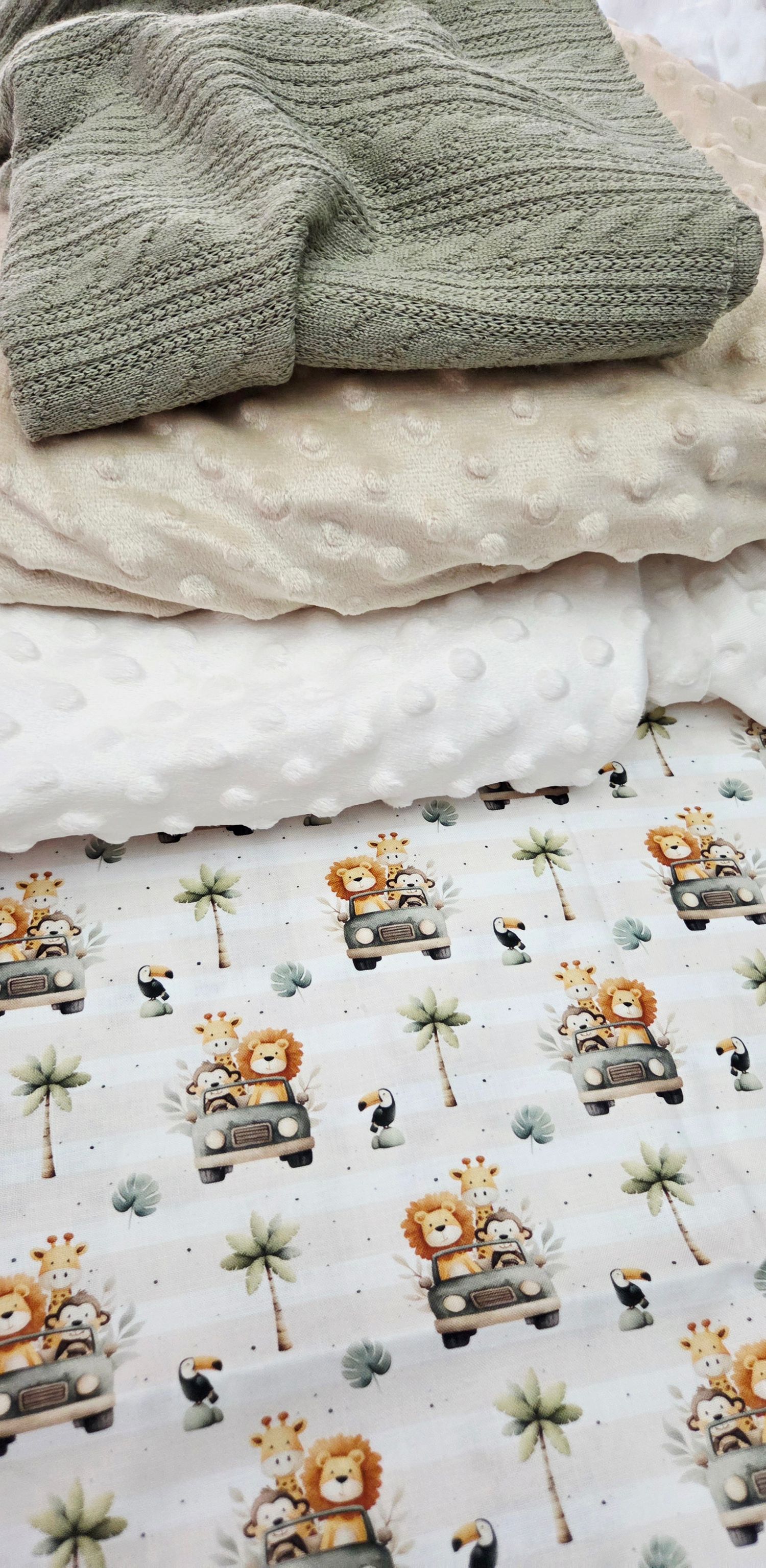 Stacked baby blankets featuring a safari animals print, cream minky dot fabric, and a sage green knit blanket.