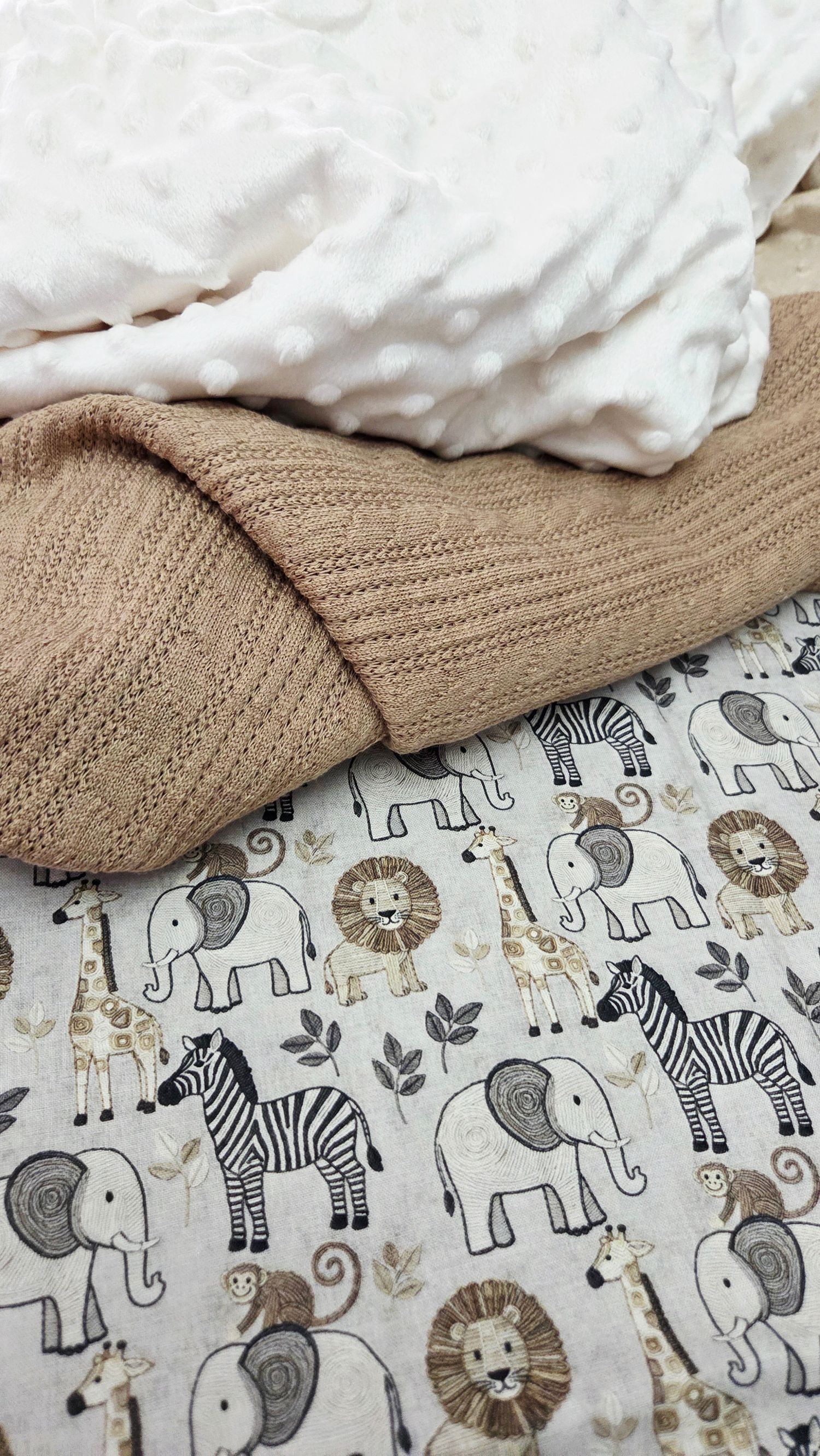 Cozy baby blankets featuring a safari animal print with elephants, zebras, lions, and giraffes alongside a knit tan blanket.
