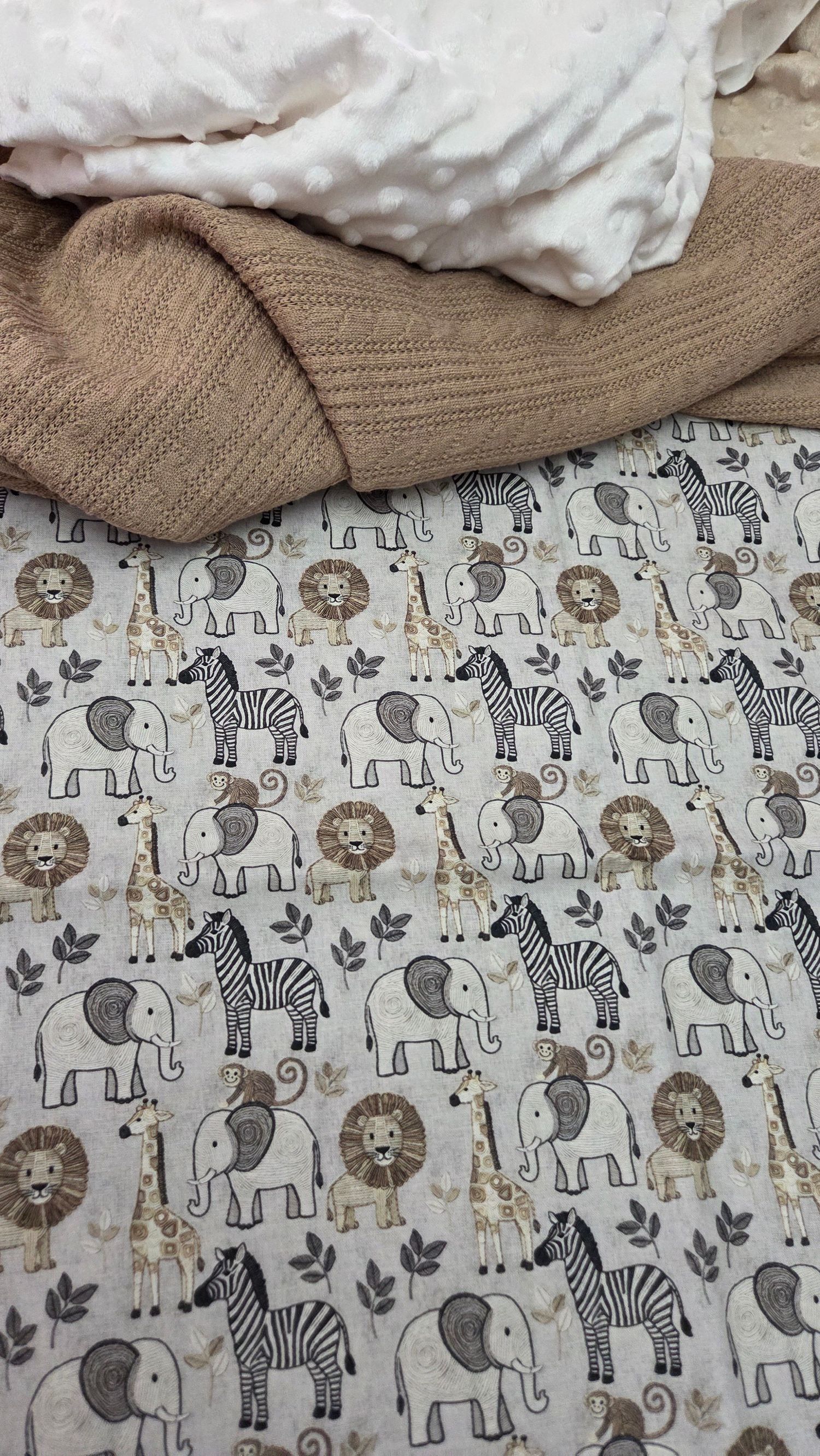 Safari animal patterned baby blanket featuring elephants, zebras, lions, and giraffes in neutral beige and gray tones.