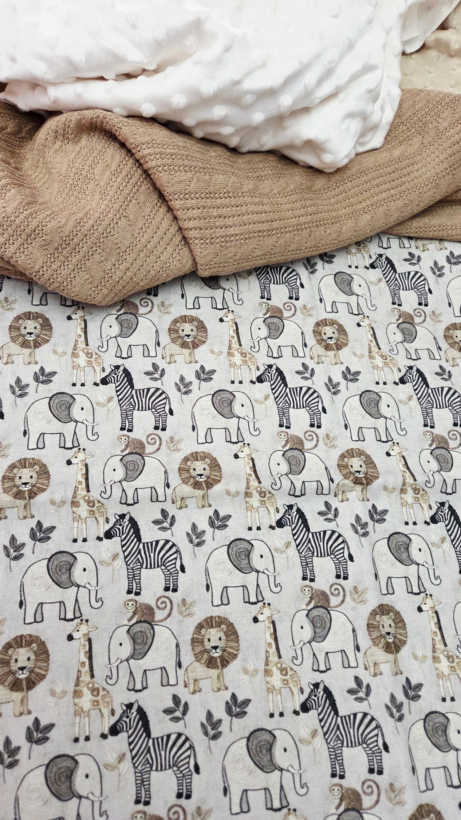 Safari animal print baby blanket featuring elephants, zebras, and lions in neutral beige and gray tones, layered with soft blankets.