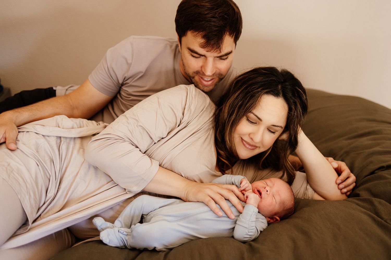 Mom and dad lay on the bed next to their newborn baby