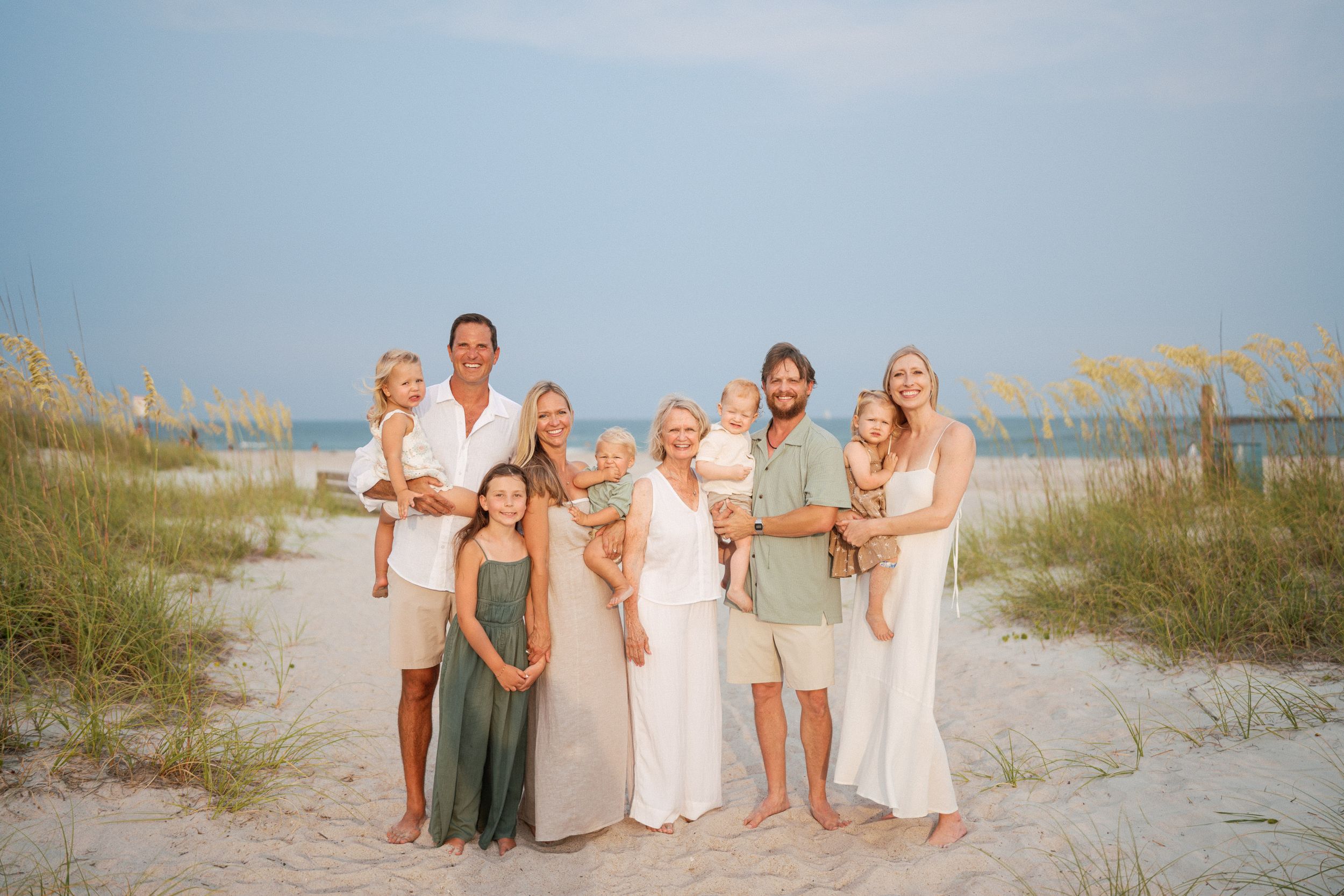 Family of eight posing together on a sandy beach with sea oats and ocean in the background.