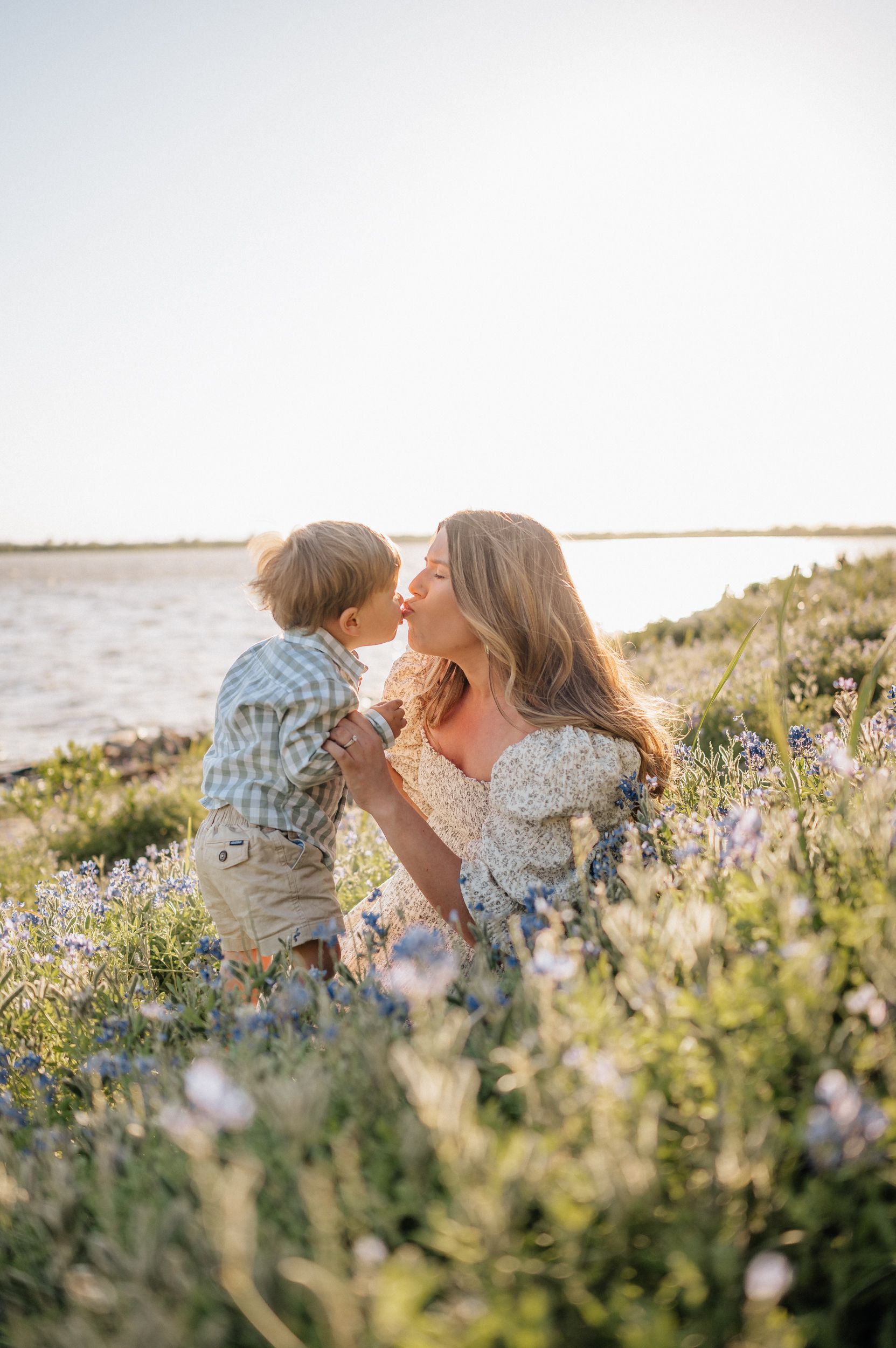 Mother and child sharing tender moment among coastal wildflowers at sunset.