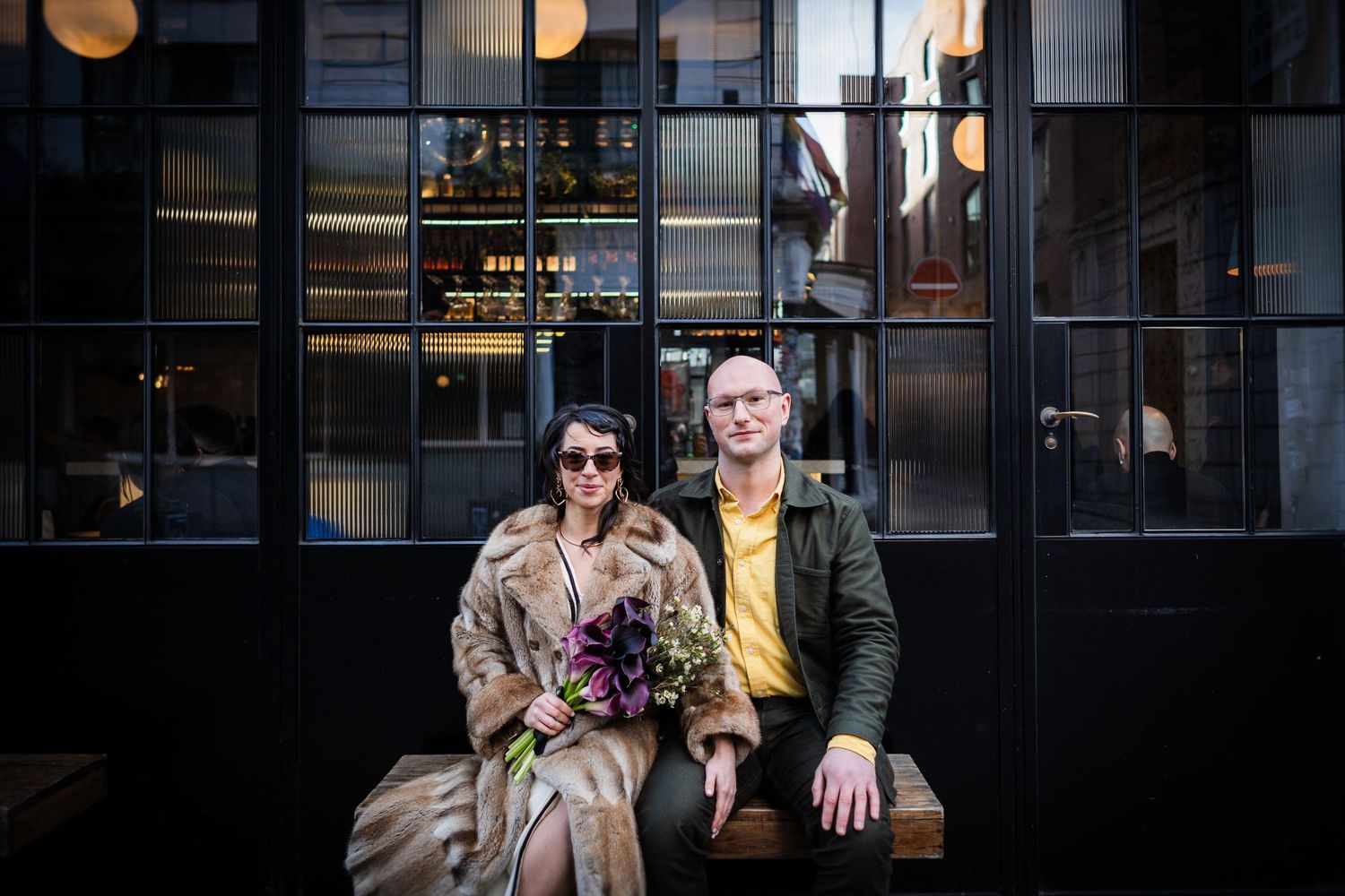 Wedding portrait captures couple with bridal bouquet in moody natural outdoor setting.