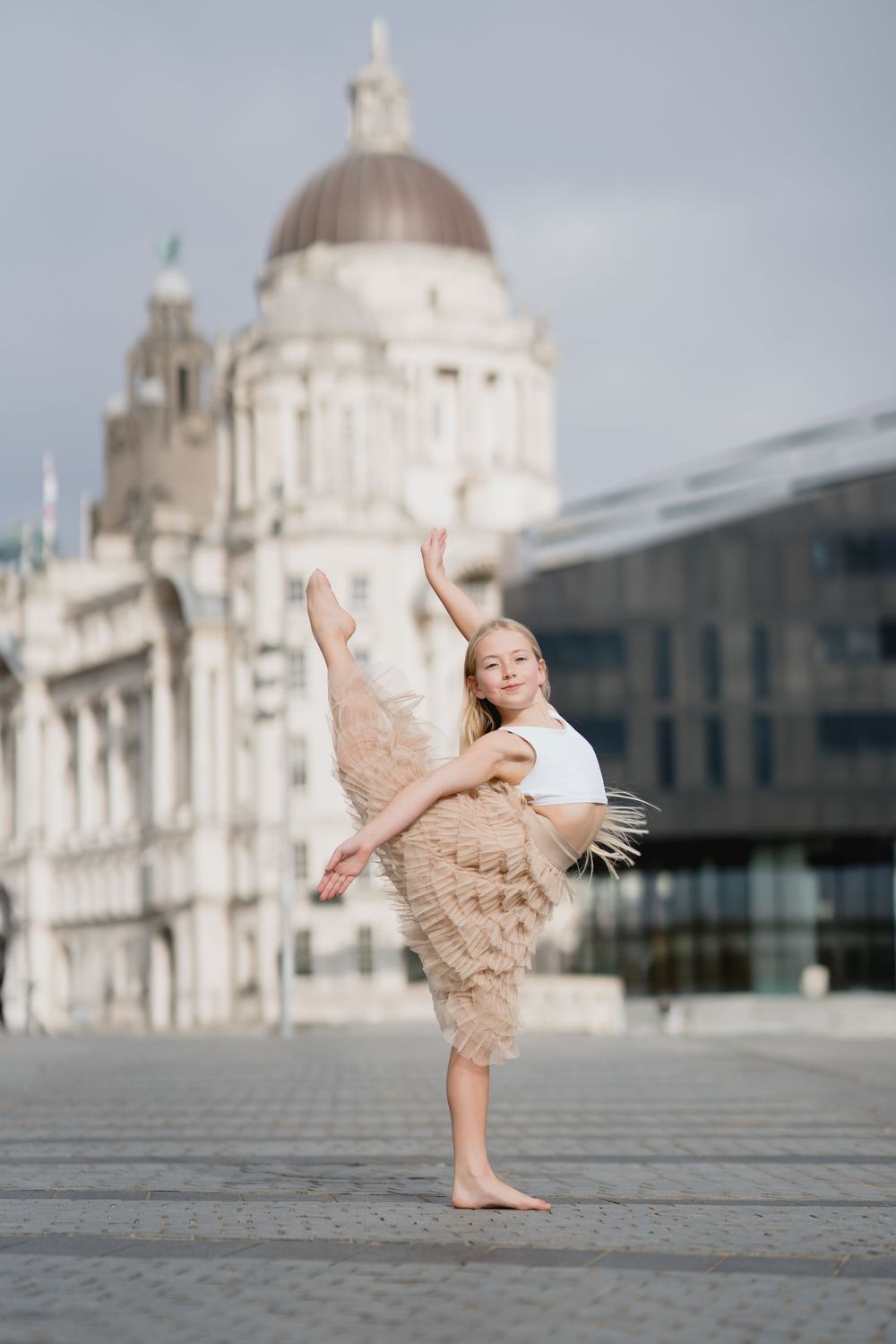 A dancer performs graceful poses in front of Liverpool's historic Pier Head buildings and the Three Graces.