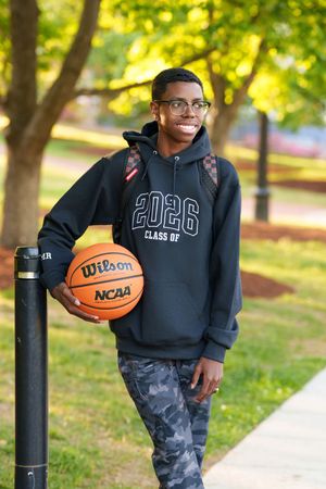 Smiling student in Class of 2026 hoodie holding Wilson NCAA basketball in a sunny park setting.