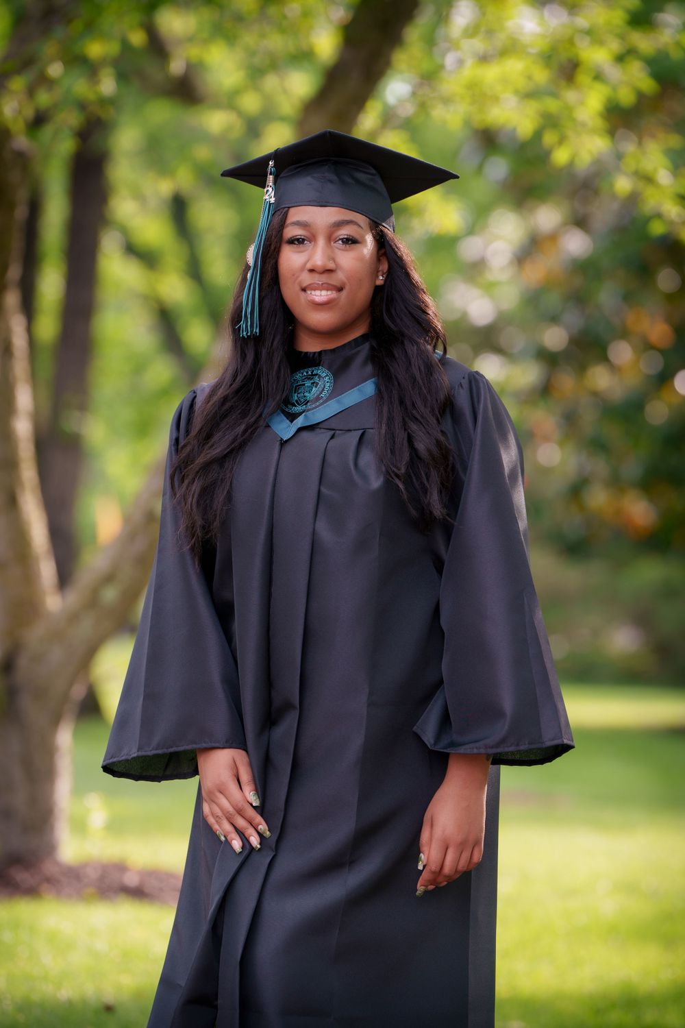 Graduate in traditional black cap and gown posing for photos in a lush green park setting.