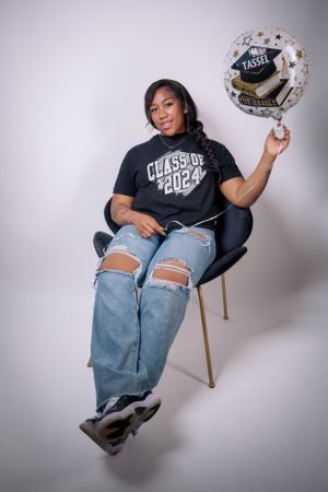 Casual photoshoot featuring someone in ripped jeans and a black t-shirt posing with graduation decorations.