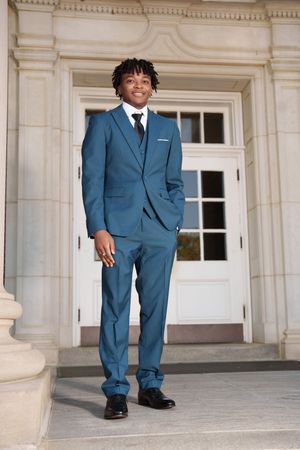 Person in blue suit standing on stone steps in front of classical building entrance.