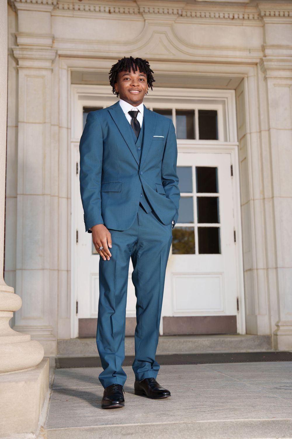 Person in blue suit standing on stone steps in front of classical building entrance.