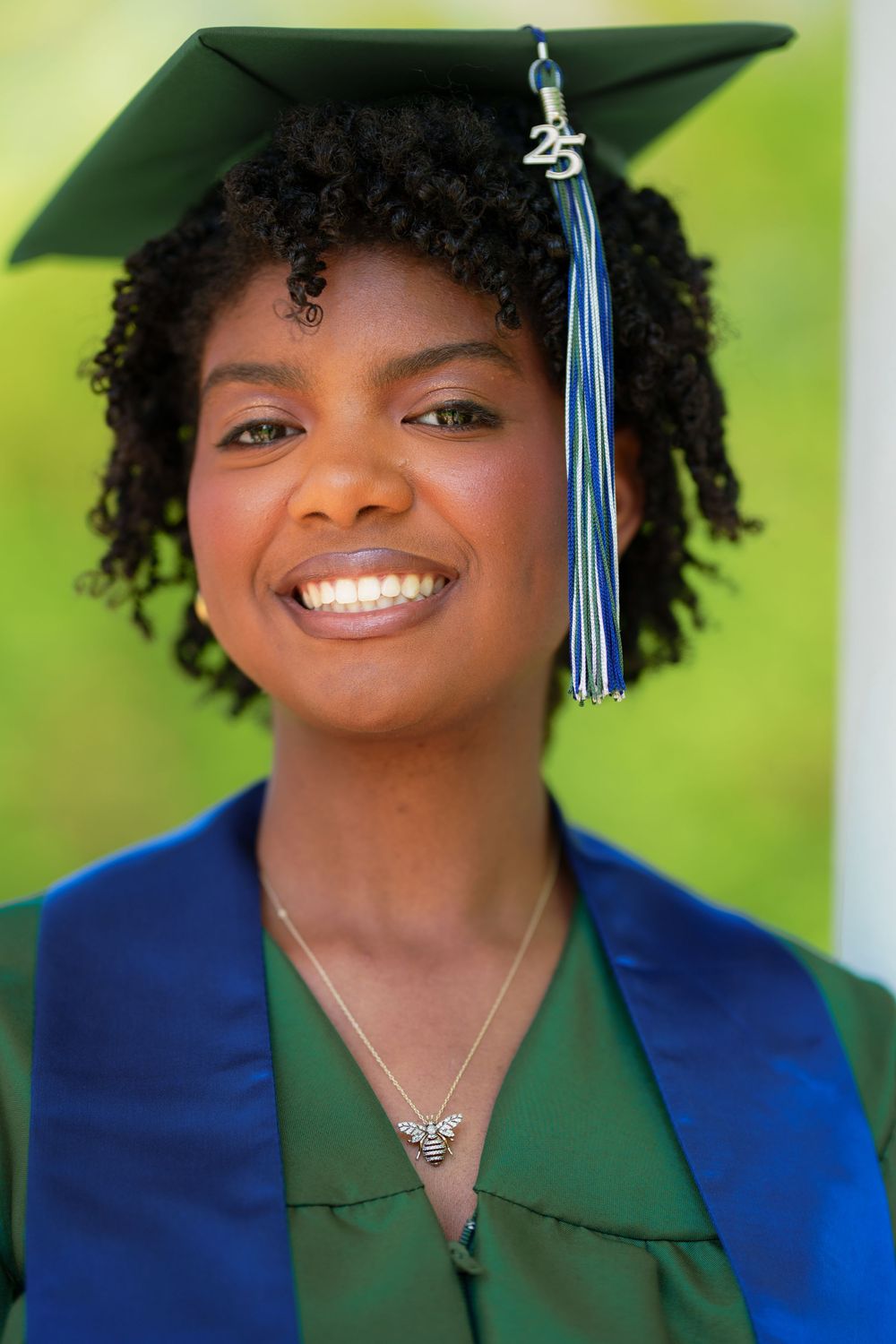 Graduate in blue and green academic regalia with graduation cap and tassel smiling at camera.