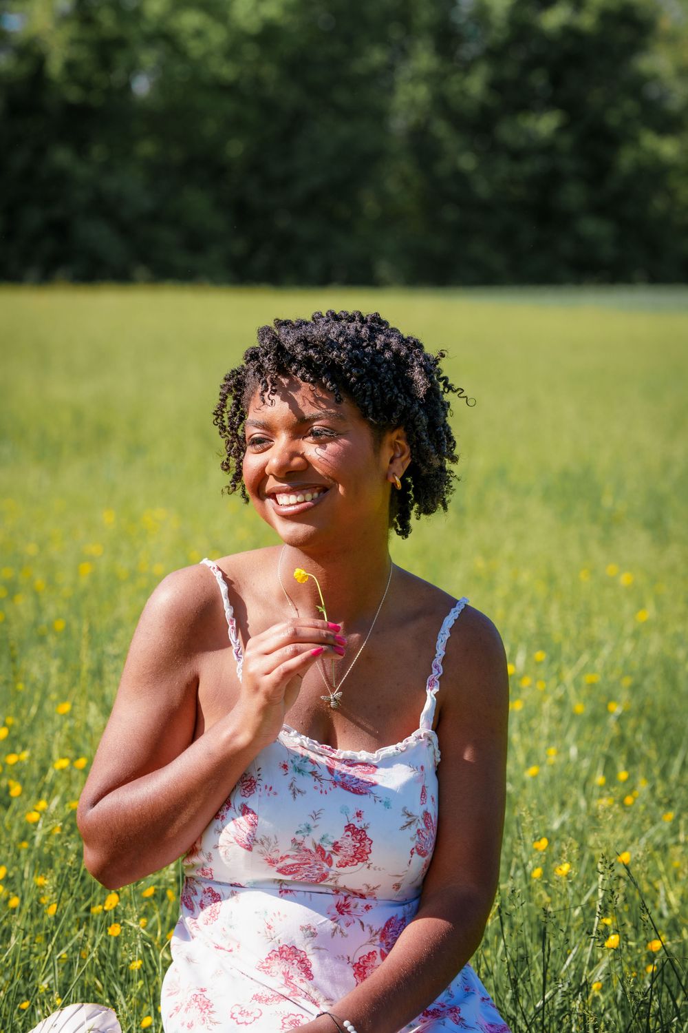 Person in floral dress sitting in sunny meadow with yellow wildflowers.