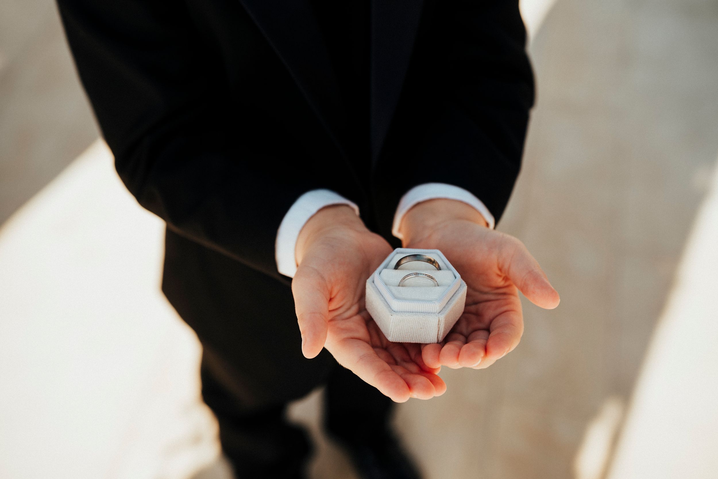 Two hands exchange a small round ring box during what appears to be a wedding ceremony.