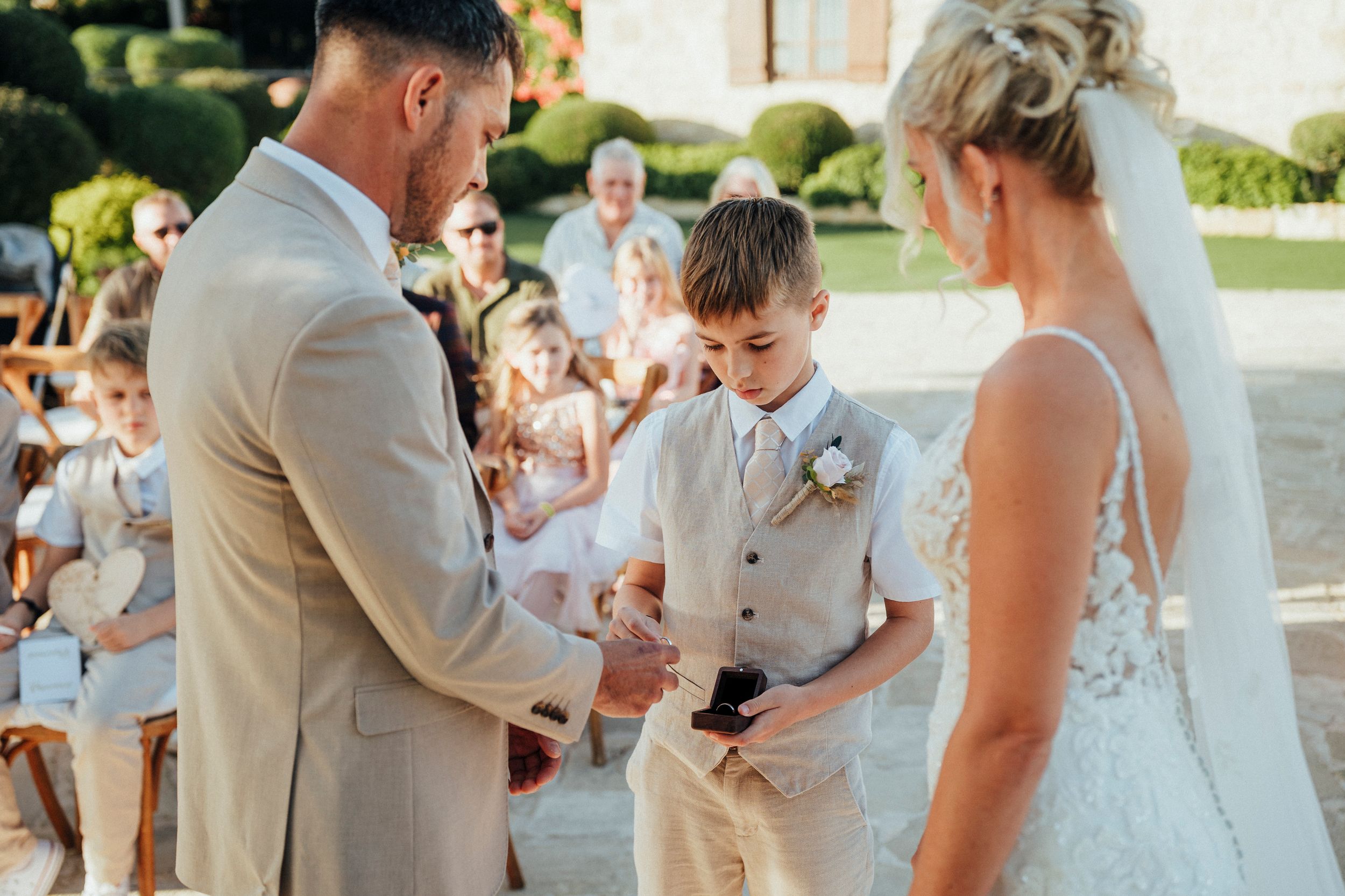 A group celebrates during an outdoor wedding ceremony with guests gathered around in a sunny garden setting.