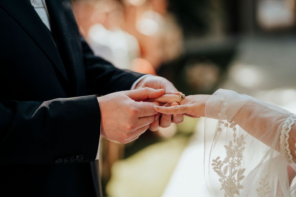 Close-up shot of hands exchanging wedding rings during a marriage ceremony with delicate lace details in view.