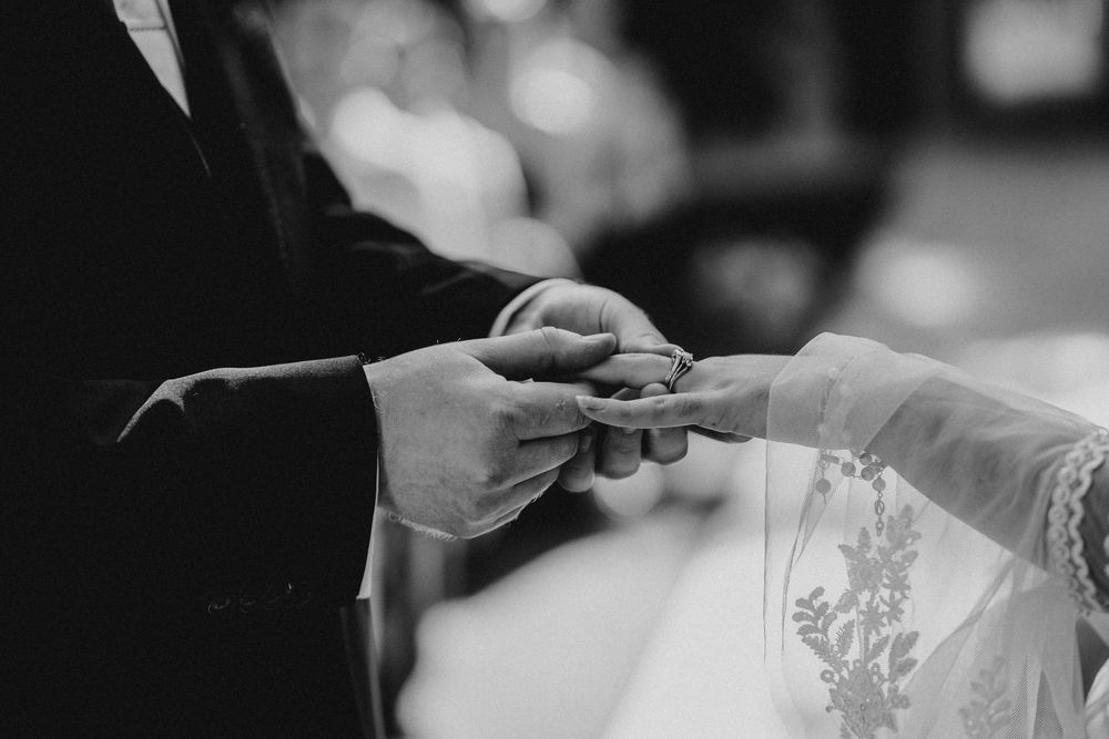 Black and white wedding photos showing hands exchanging rings and tender moments during a ceremony.