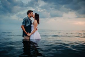 A romantic couple embraces in the ocean waters during sunset creating a dreamy silhouette against the horizon.