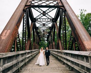 A series of rustic wedding photos taken on a historic iron railroad bridge with wooden planks and geometric trusses.