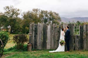 A couple shares a romantic moment by a rustic wooden fence with mountains and trees in the background.