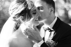 A tender black and white wedding moment captured as the groom kisses his bride's cheek during their special day.