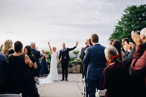 Wedding guests cheer and raise their arms in celebration during an outdoor ceremony by the water.