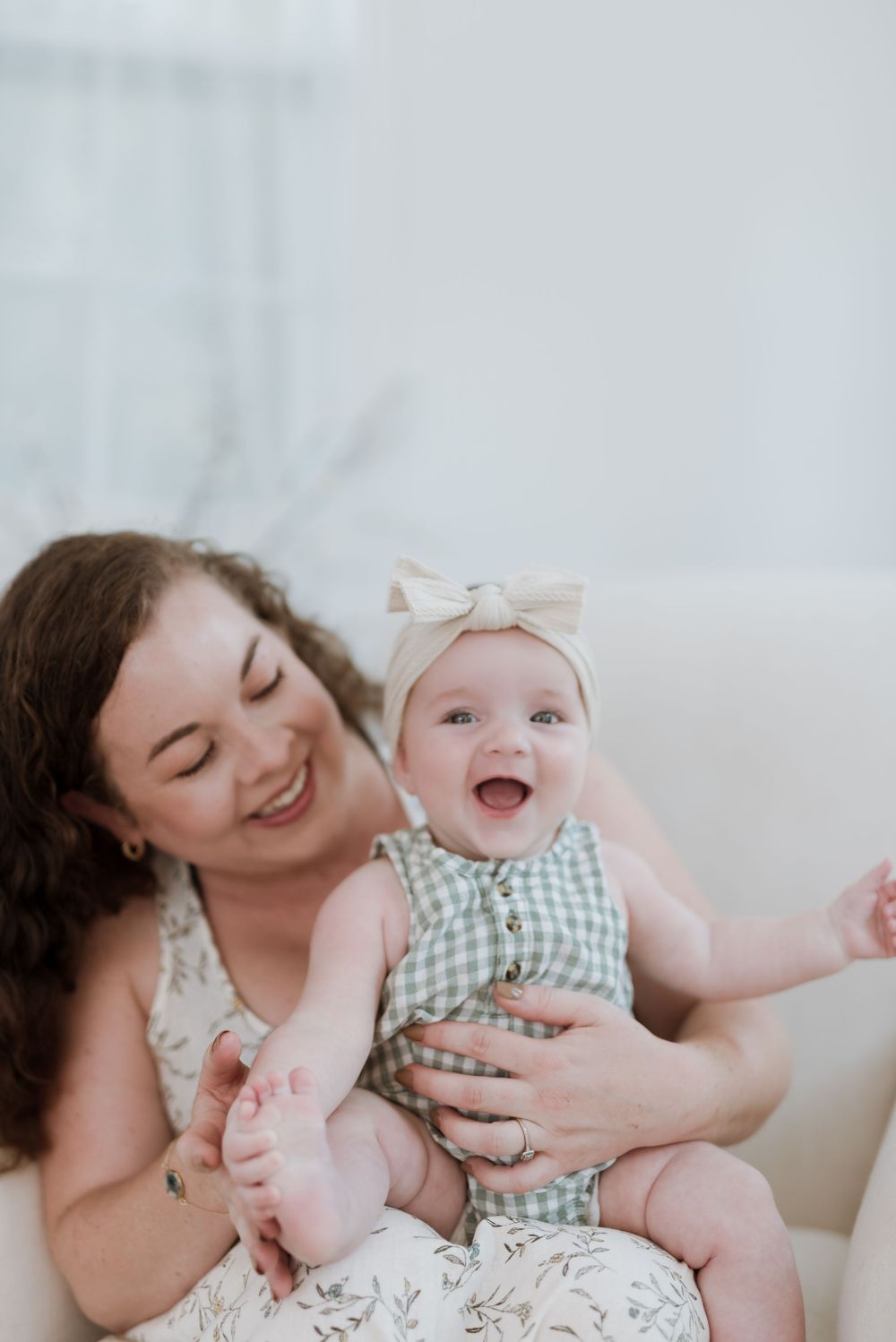 A joyful mother shares tender moments with her laughing baby during a light and airy indoor photo session.