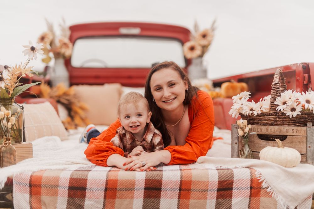 A red vintage truck serves as a rustic backdrop for a fall-themed outdoor setting with checkered blankets and pumpkins.