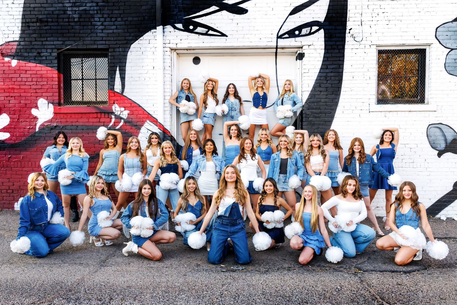 Group wearing blue and white outfits sit together against white wall for coordinated outdoor photo shoot.