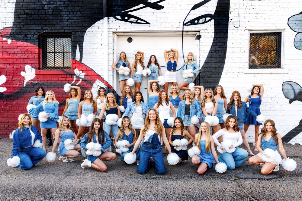 Group wearing blue and white outfits sit together against white wall for coordinated outdoor photo shoot.