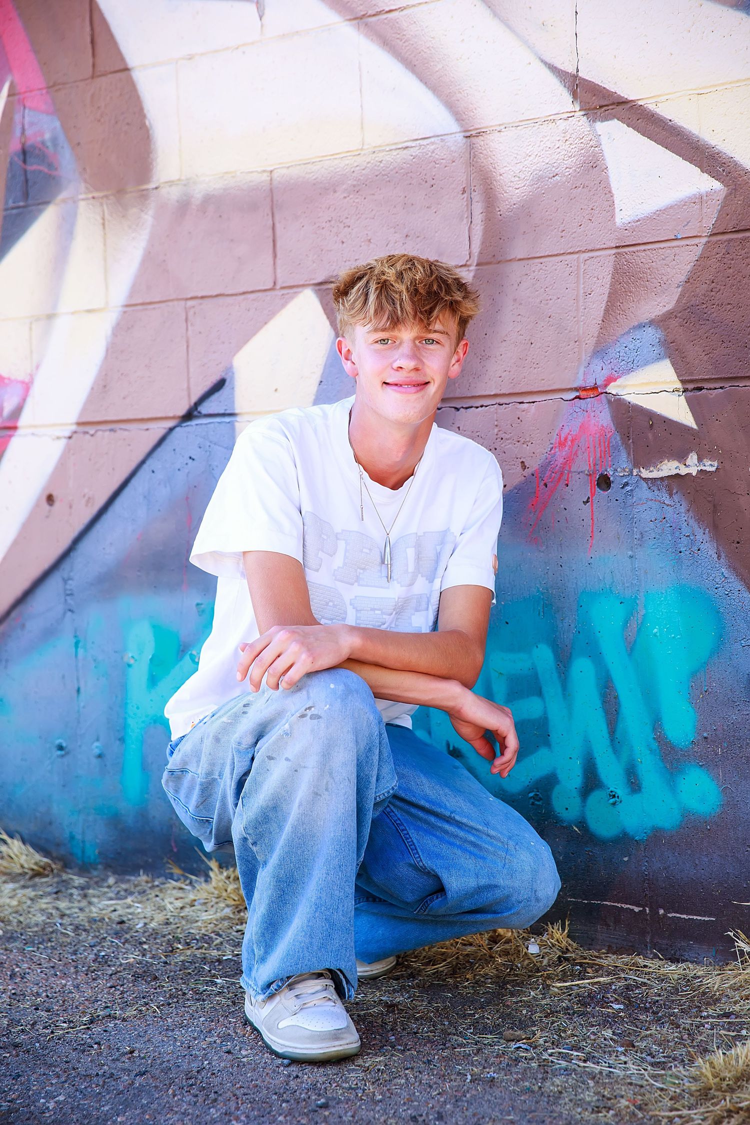 Person in blue jeans and white t-shirt sits casually against graffiti wall with urban street art background.