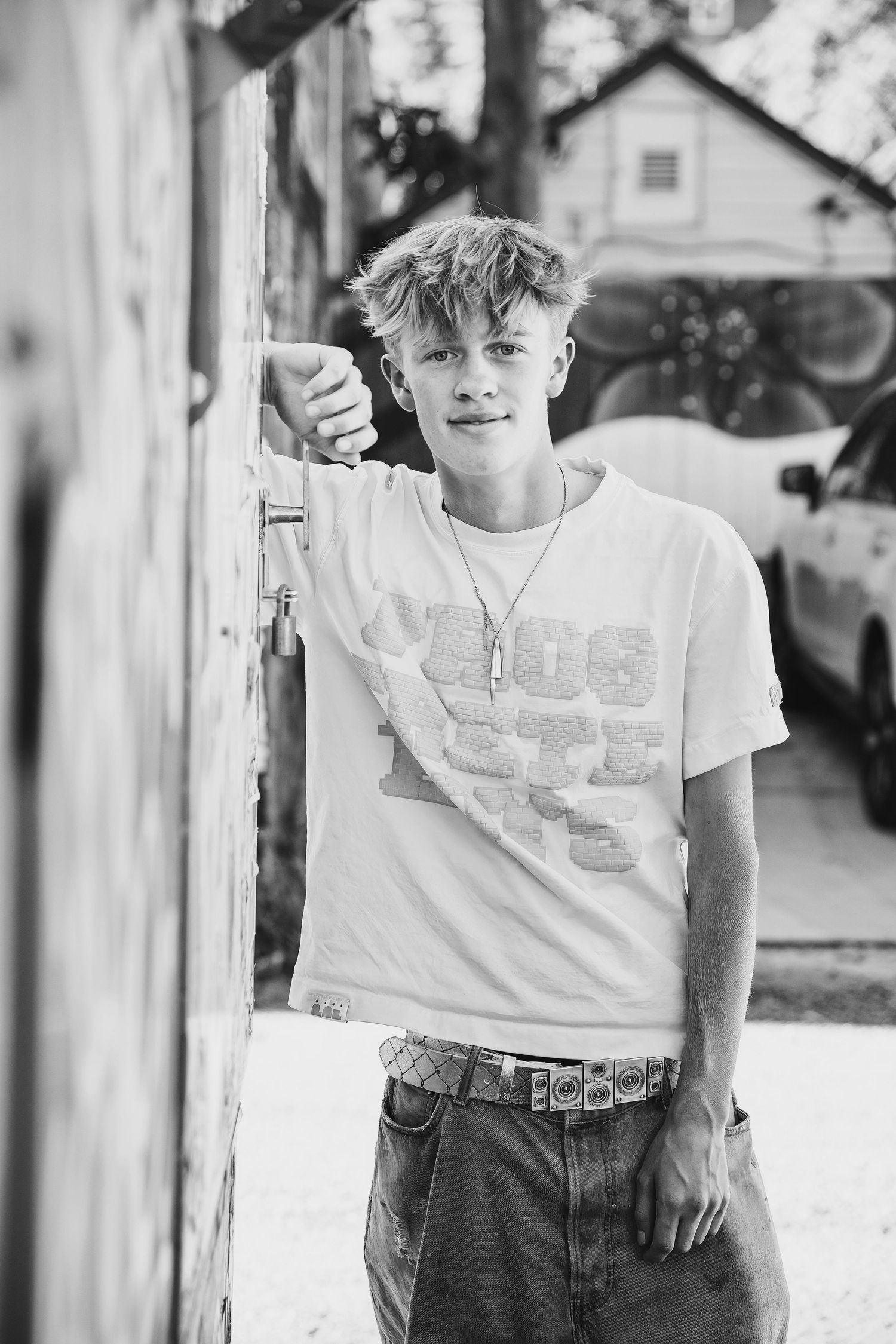 Black and white portrait photo of someone leaning against a wall wearing a white t-shirt and jeans in a casual pose.