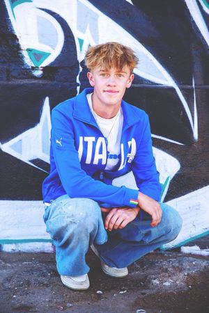 Person in blue hoodie crouches against black and white graffiti wall.