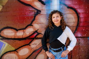 A young person in color-blocked black and white sweater poses against a vibrant graffiti wall.
