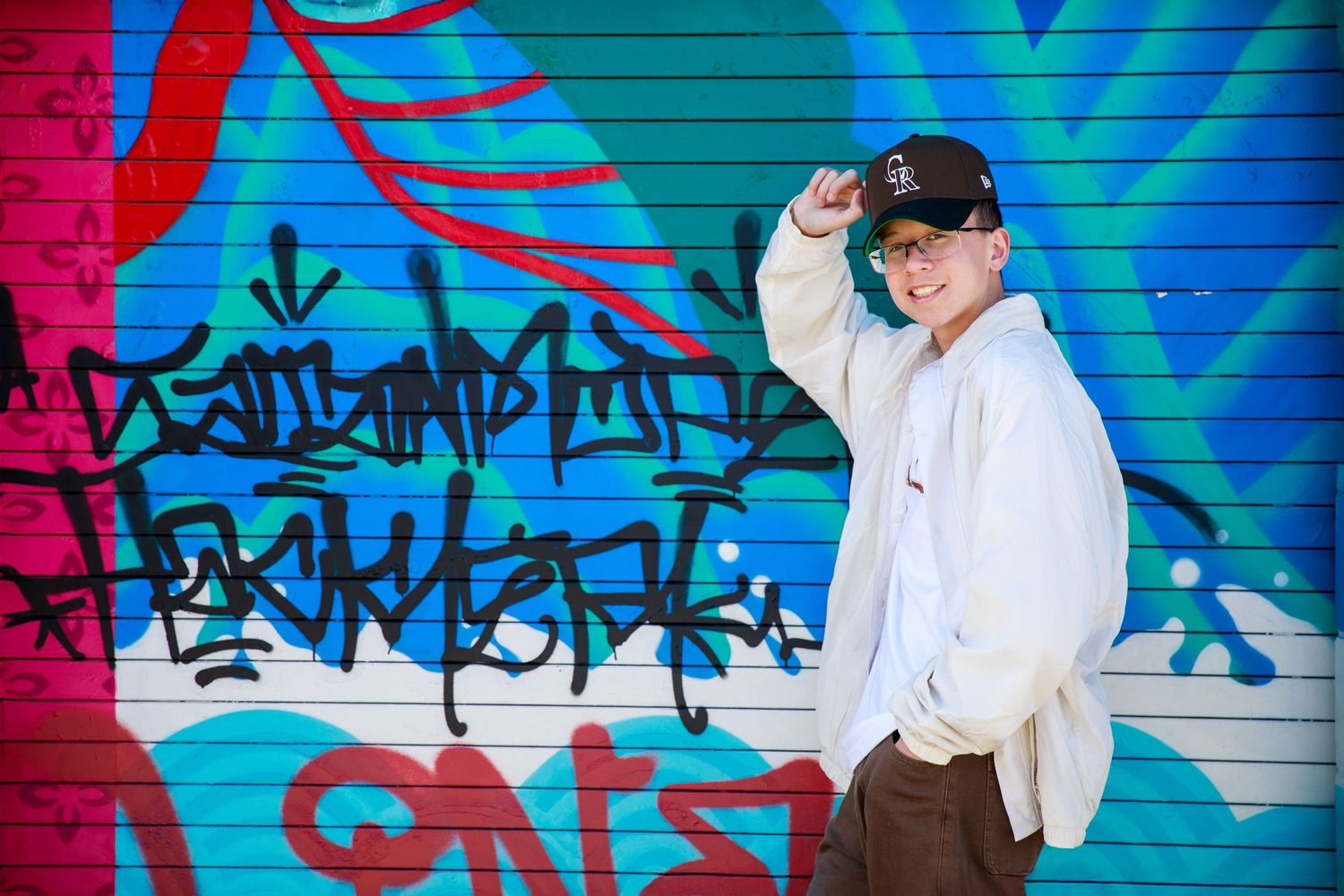 A series of photos captured against a vibrant blue and red graffiti wall shows playful poses and dancing movements.