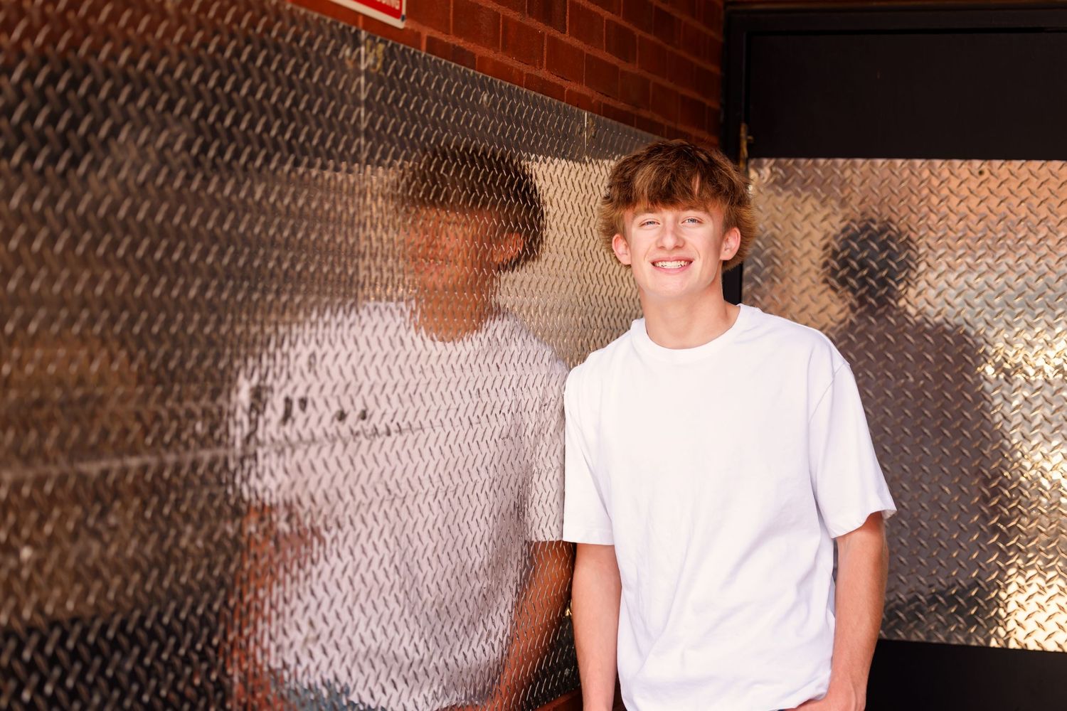 Two young boys in white t-shirts smiling in front of a metallic diamond plate wall backdrop.