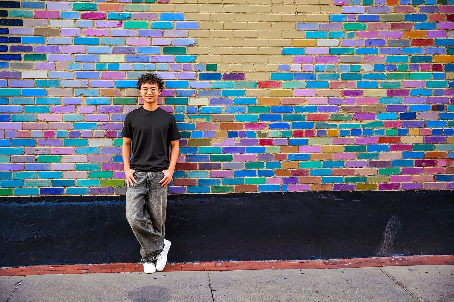 Colorful graffiti wall with rainbow-colored bricks creates vibrant backdrop for urban street photography.