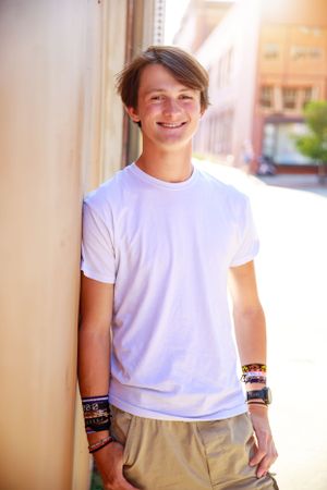 Casual portrait of young person in white t-shirt and beige pants against light wall.