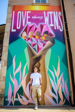 Person posing in front of colorful street art mural featuring geometric diamond and floral designs.