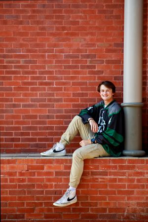 Person in striped hoodie and khakis sitting casually on brick ledge wearing sneakers.