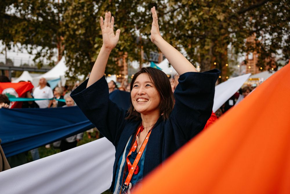 Person raising arms in celebration at outdoor event with orange banner.