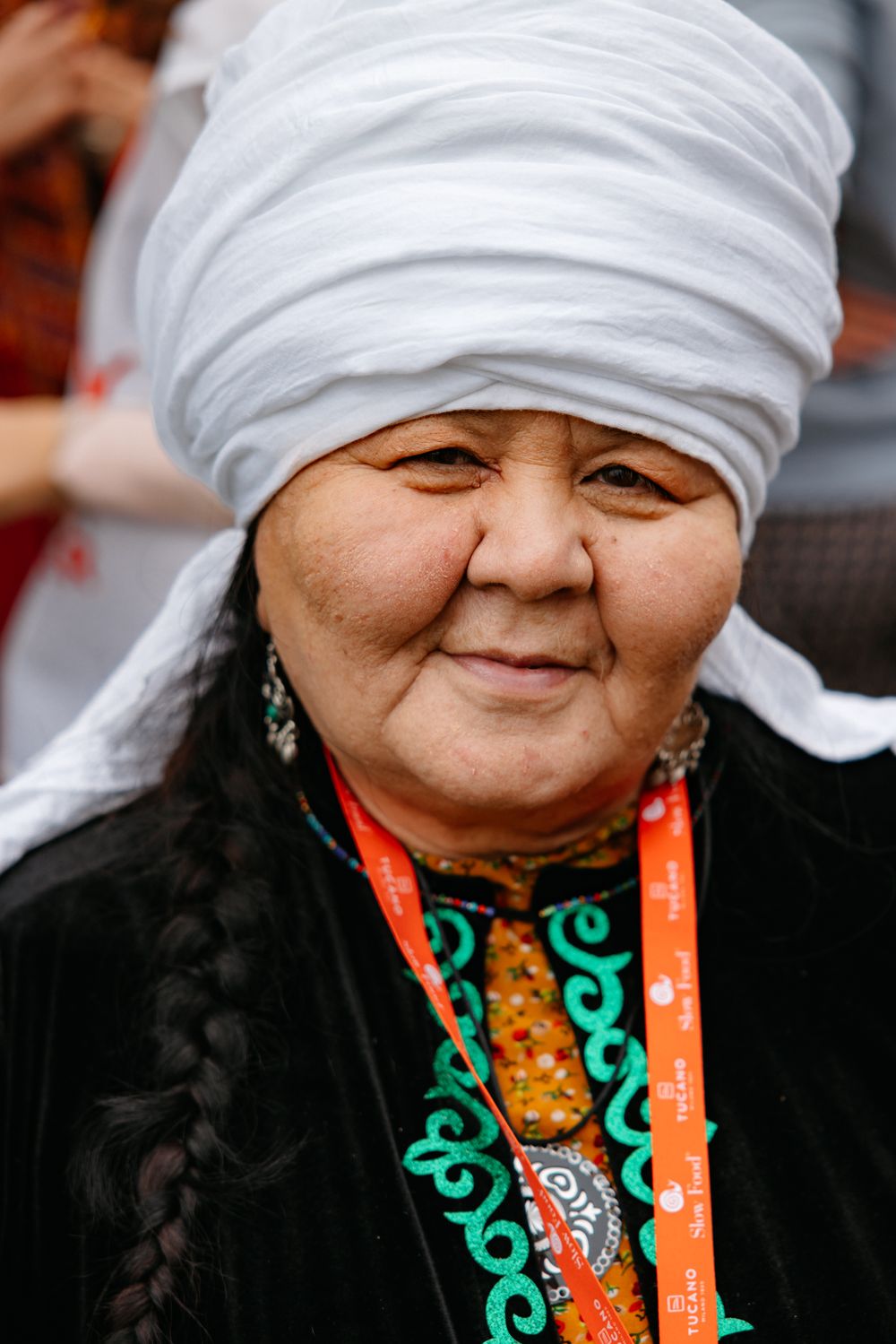 Woman in traditional dress with white headwrap and ornate jewelry smiling.