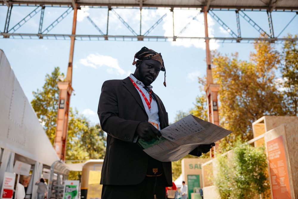 Professional figure in a dark suit and tie reviewing documents outdoors under an industrial structure.