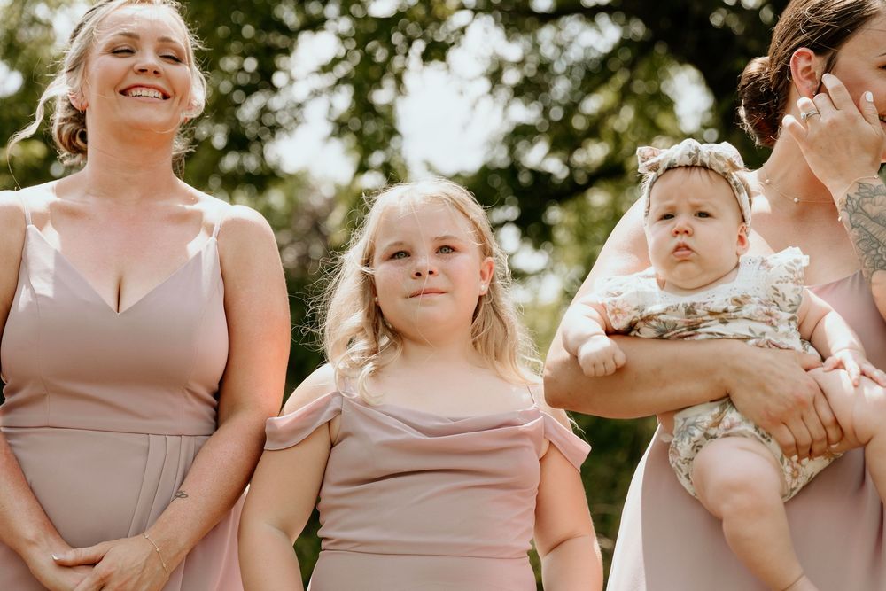 Several bridesmaids in pale pink dresses hold adorable puppies outdoors during a wedding photoshoot.