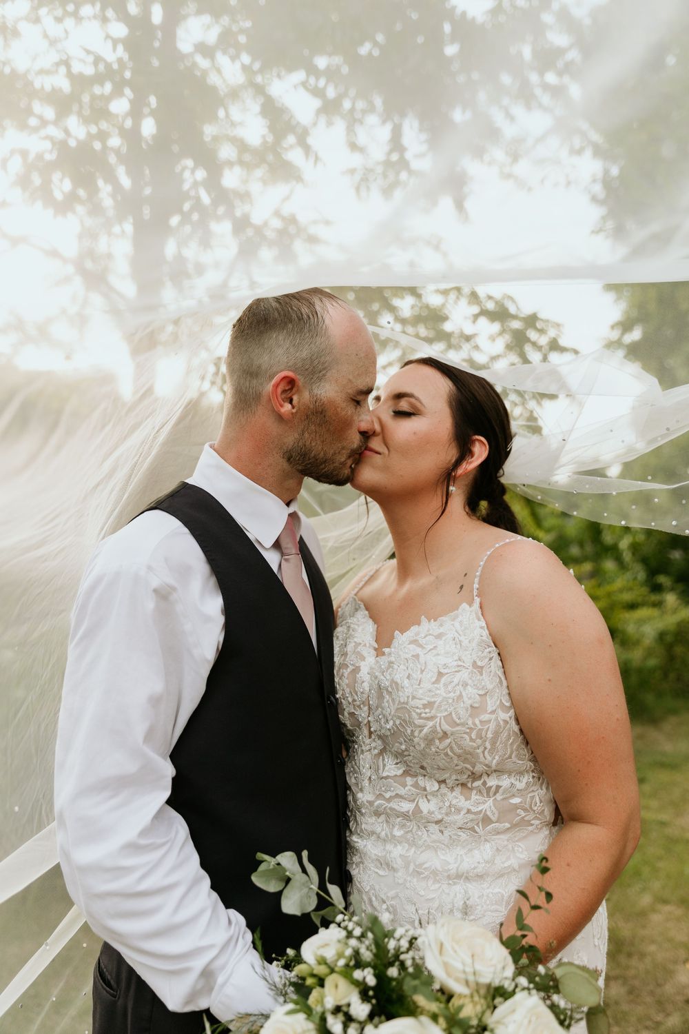A romantic wedding moment captured outdoors as a couple shares a tender kiss under a flowing veil.
