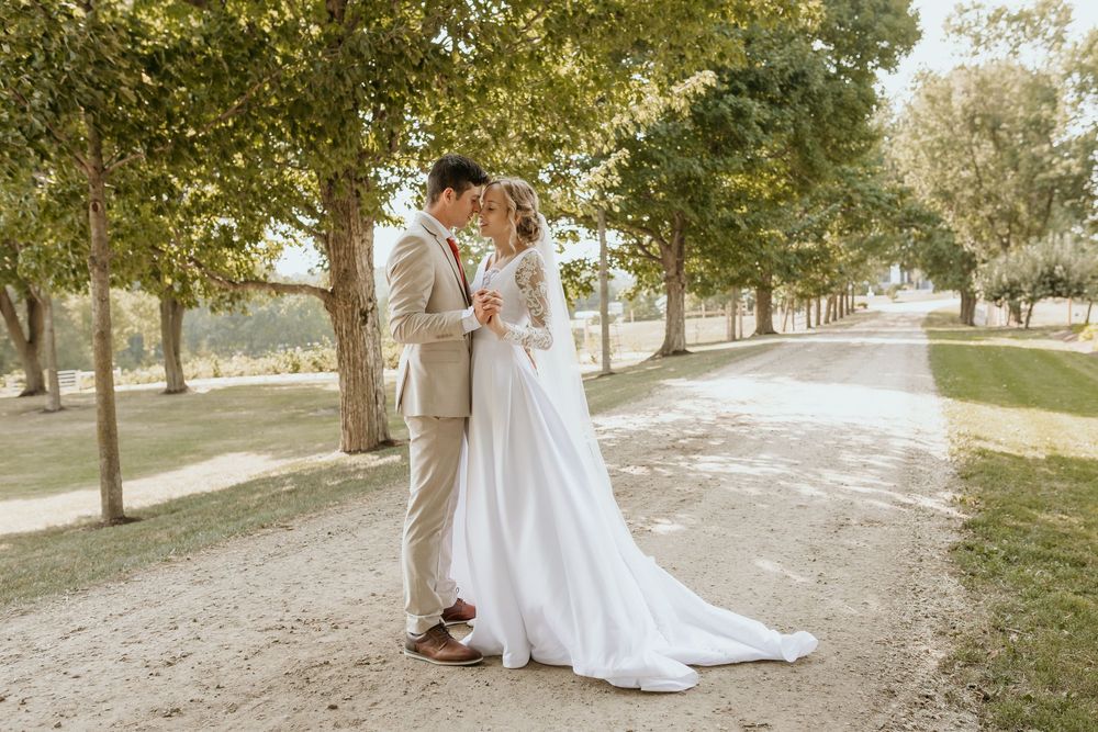 A wedding couple stands together on a tree-lined pathway in the golden afternoon sunlight.